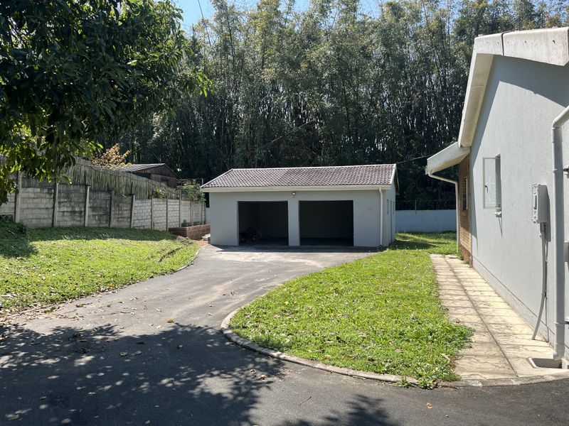 A detached double garage with a tiled roof, situated at the end of an asphalt driveway within a landscaped residential yard.
