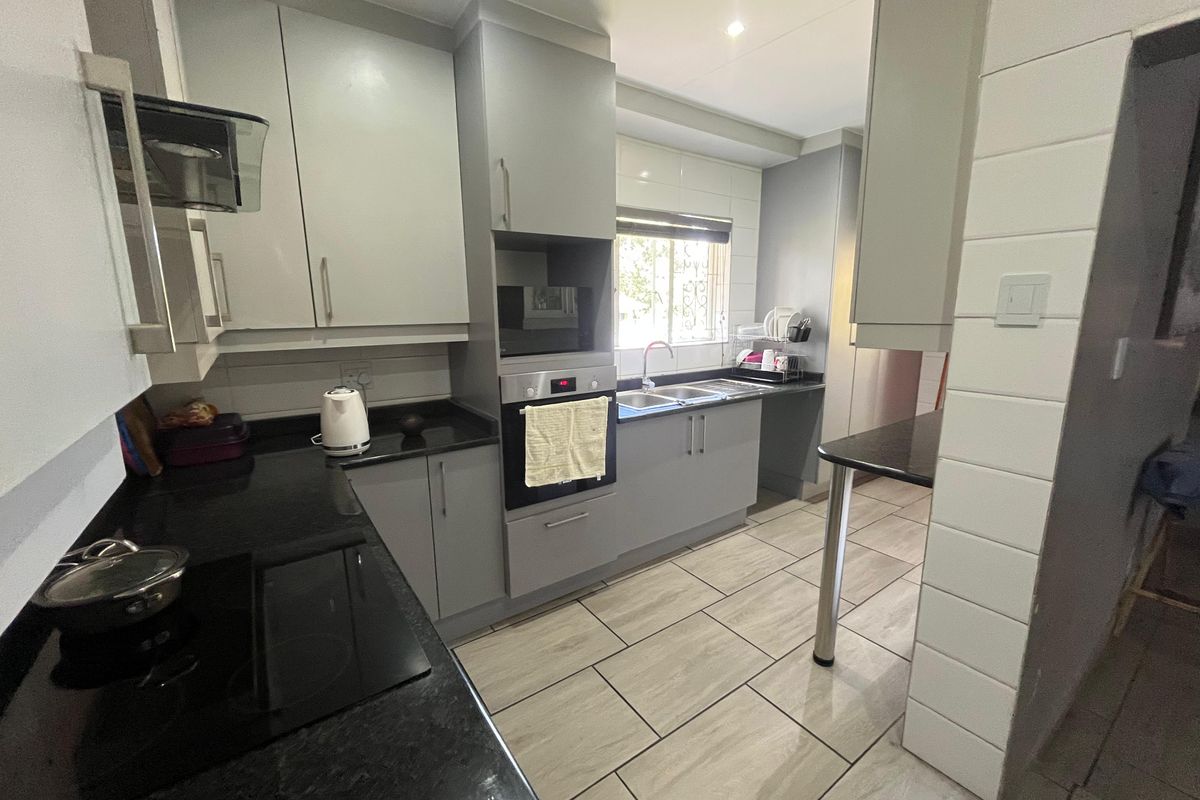 Modern kitchen featuring grey cabinetry, black granite countertops, built-in oven, electric hob, and tiled flooring with a functional layout.