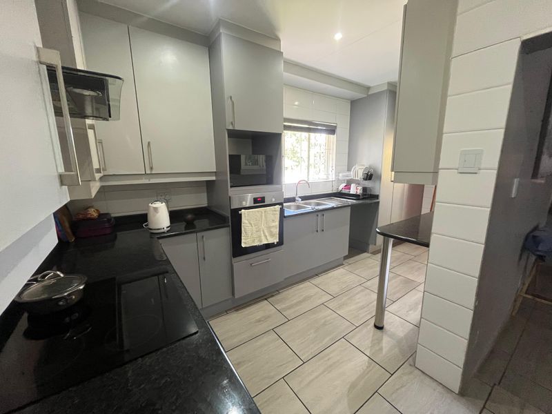Modern kitchen featuring grey cabinetry, black granite countertops, built-in oven, electric hob, and tiled flooring with a functional layout.
