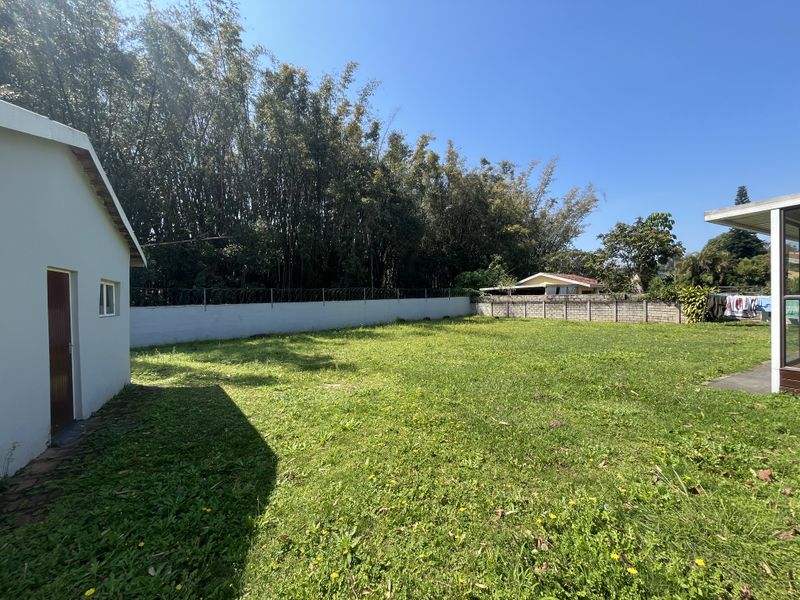 A spacious backyard featuring a large lawn area, enclosed by a perimeter wall with security razor wire.