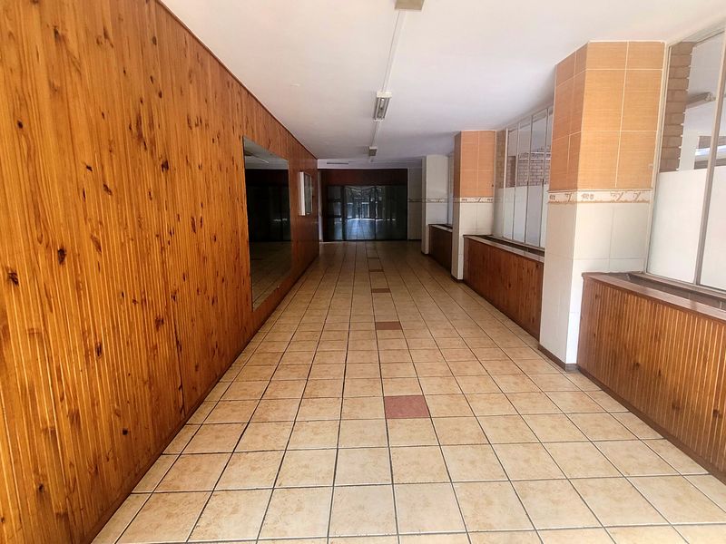 A long, vacant hallway featuring dated wood paneling, tiled flooring, and built-in cabinetry, offering a blank canvas for modernization.