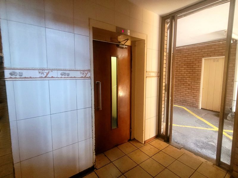 A functional building hallway featuring an elevator access point, tiled wall finishes, and direct access to an external walkway area.