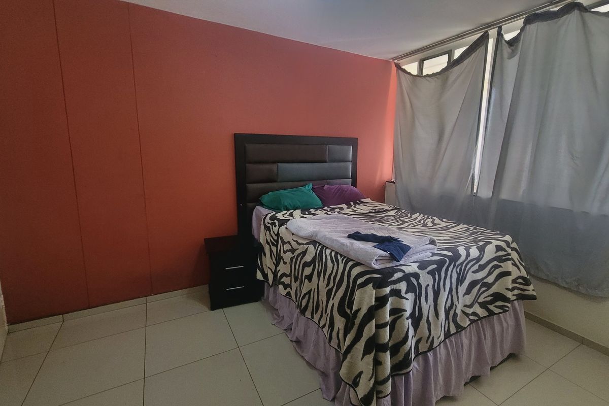 A bedroom featuring tiled flooring and large windows, providing natural light to the space.