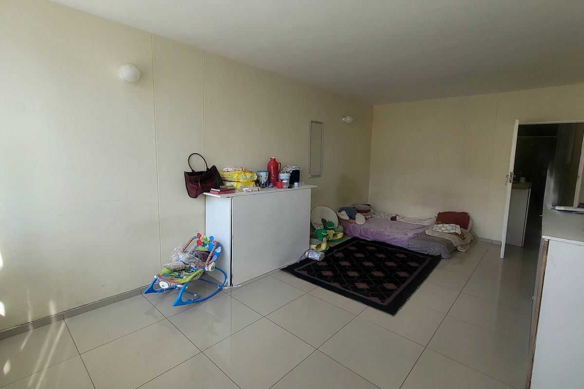 A spacious living area featuring neutral tiled flooring and wall-mounted lighting, offering a blank canvas for interior design and furniture arrangement.