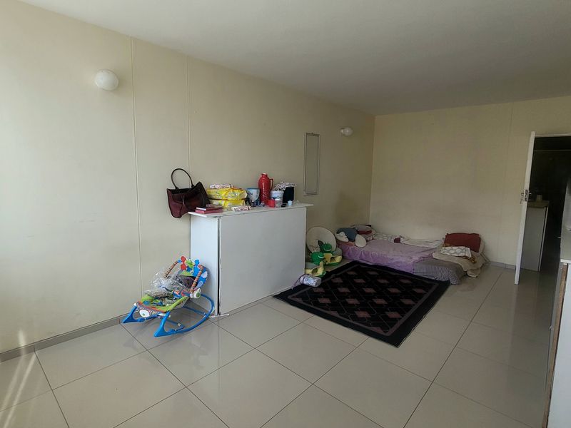 A spacious living area featuring neutral tiled flooring and wall-mounted lighting, offering a blank canvas for interior design and furniture arrangement.