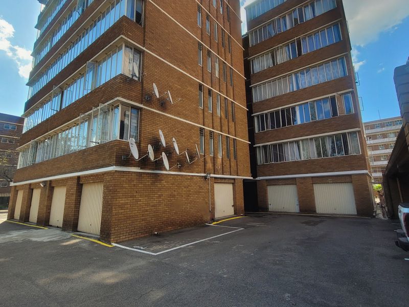 Exterior view of a multi-story face-brick apartment building featuring multiple ground-level garages and steel-framed windows.