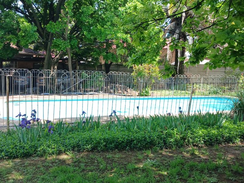 A backyard swimming pool area featuring a paved surround and protective metal fencing, set within a mature garden environment.