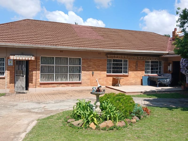 Rear view of a single-story brick house featuring a tiled roof, paved patio area, and established garden space.