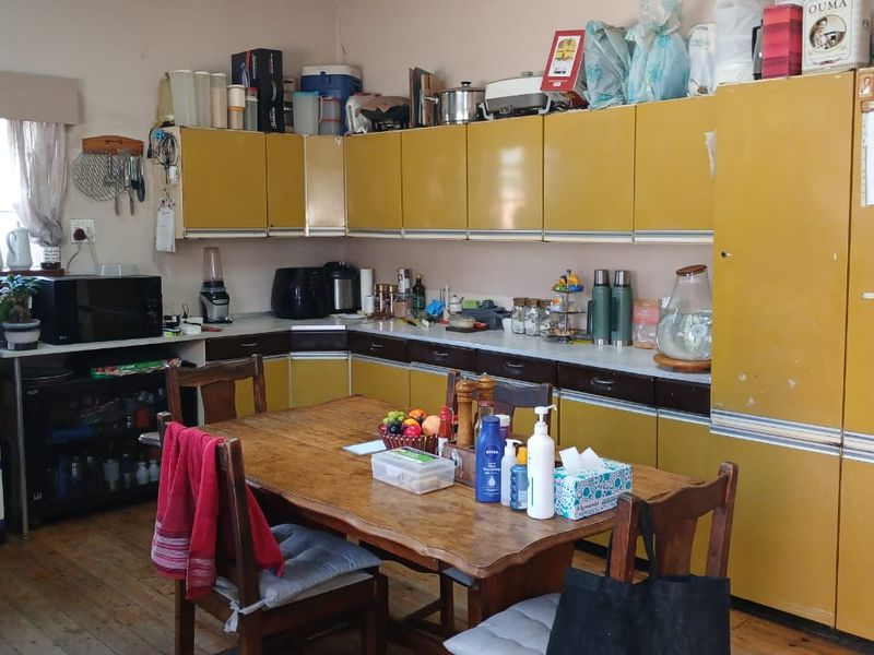 A dated kitchen featuring original yellow laminate cabinetry, laminate countertops, and timber flooring, offering significant potential for a modern renovation.