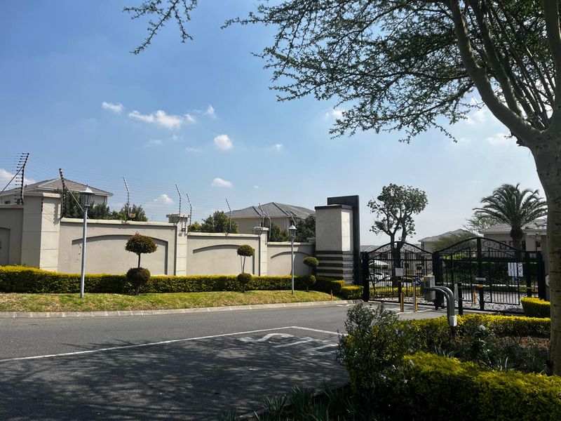 Front entrance view of the apartment complex featuring a secure perimeter wall with electric fencing, wrought iron gates, and well-maintained landscaped garden areas.