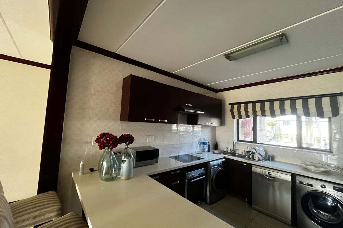 A functional kitchen featuring dark cabinetry, a breakfast bar, tiled backsplash, and integrated appliances including a hob, oven, and dishwasher.