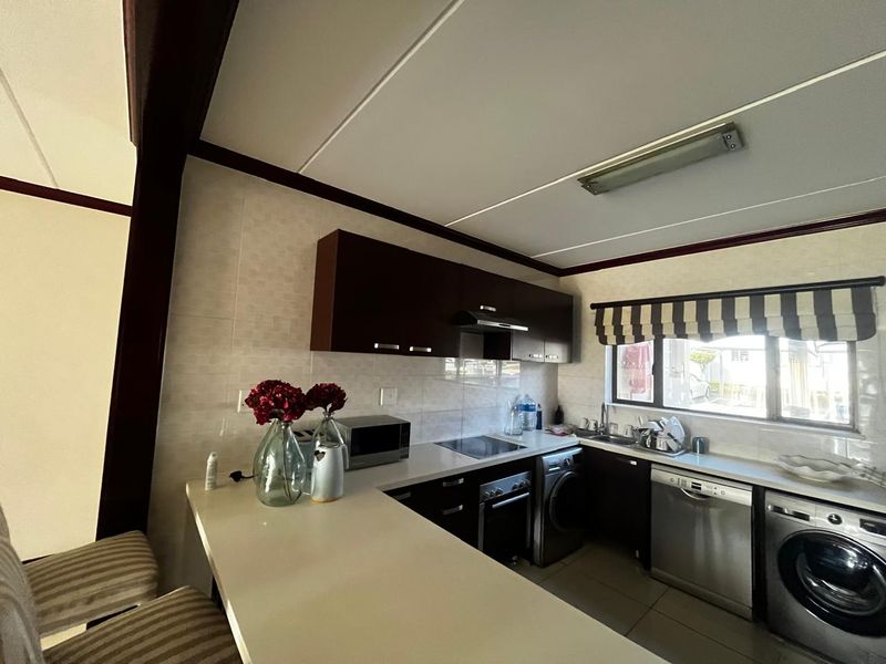 A functional kitchen featuring dark cabinetry, a breakfast bar, tiled backsplash, and integrated appliances including a hob, oven, and dishwasher.