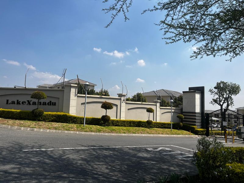 The entrance facade of Lake Xanadu estate featuring a secure perimeter wall with electric fencing and landscaped garden beds.