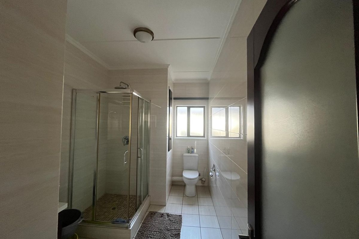 A functional bathroom featuring a glass shower enclosure, a standard toilet, and neutral wall and floor tiling.