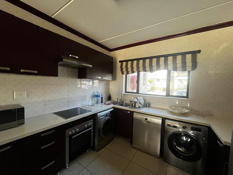 A functional kitchen featuring dark wood cabinetry, tiled backsplash, built-in oven, hob, extractor fan, and integrated laundry and dishwasher appliances.