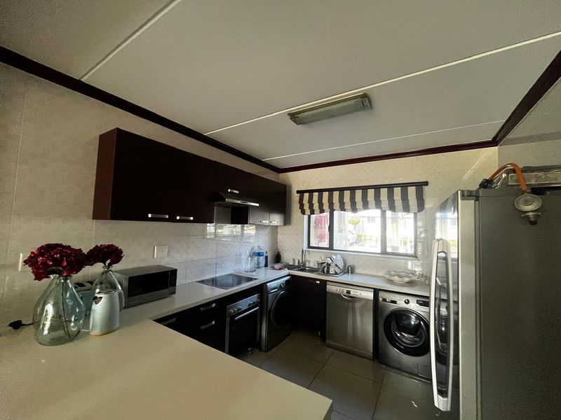 A functional kitchen featuring dark built-in cabinetry, a tiled backsplash, integrated oven and hob, and dedicated spaces for laundry appliances.