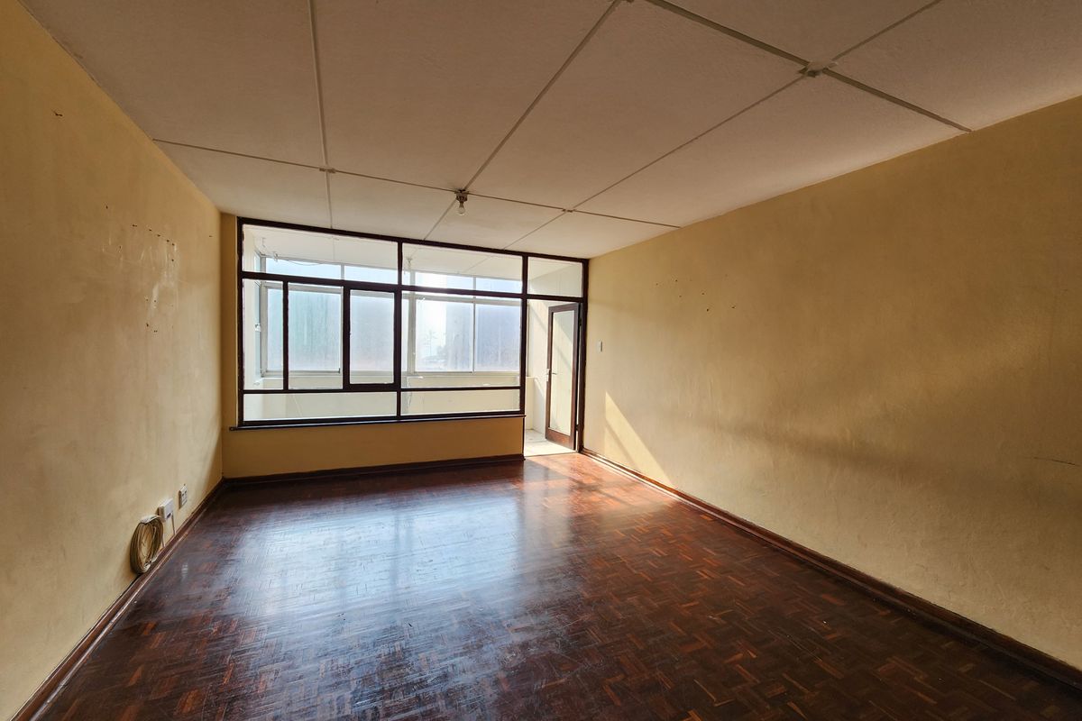 An empty living room featuring original parquet flooring, large windows providing natural light, and access to an adjoining balcony area.