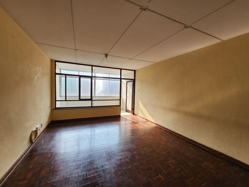 An empty living room featuring original parquet flooring, large windows providing natural light, and access to an adjoining balcony area.