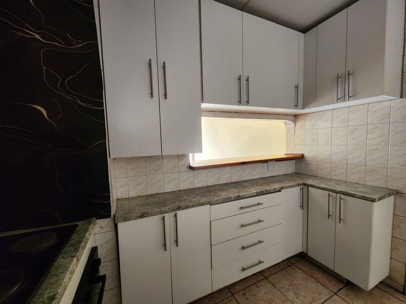 A functional kitchen featuring white cabinetry, laminate countertops, a tiled backsplash, and built-in cooking appliances, offering a clean and practical workspace.