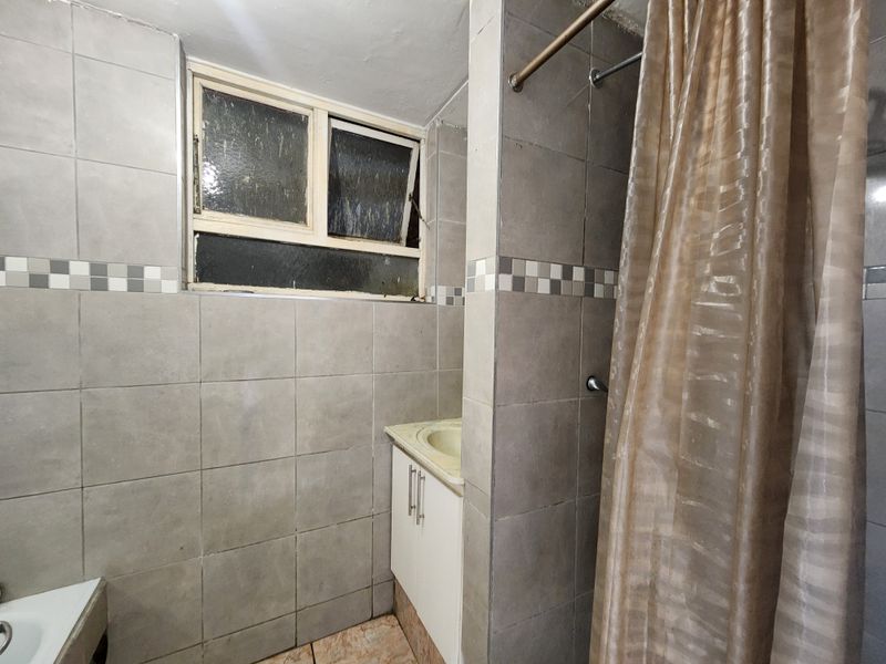 A dated bathroom featuring tiled walls, a vanity cabinet with an integrated basin, and a shower area with a curtain rail.