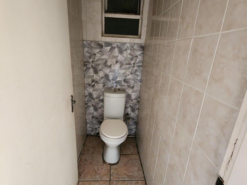 A compact guest bathroom featuring tiled walls and flooring with a standard toilet and window.
