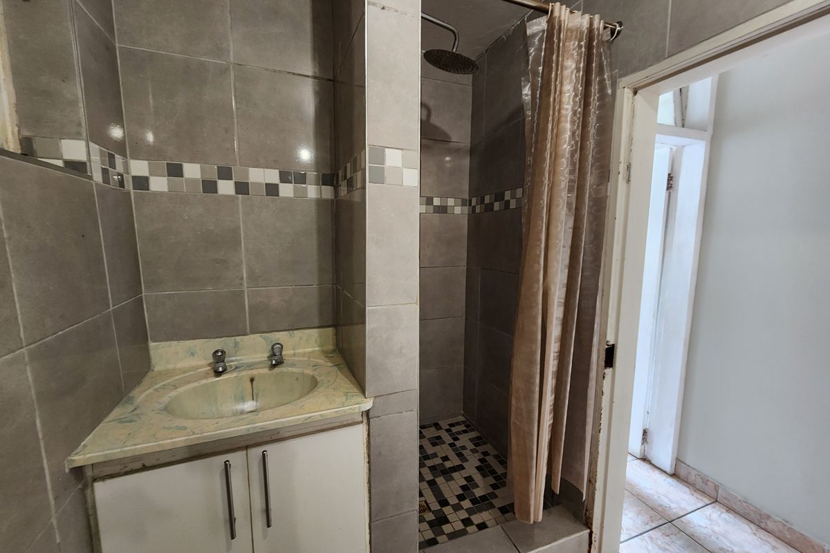 A compact bathroom featuring a tiled shower enclosure, vanity cabinet with basin, and neutral wall tiling. The space requires minor cosmetic updates.
