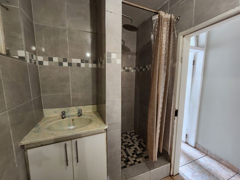 A compact bathroom featuring a tiled shower enclosure, vanity cabinet with basin, and neutral wall tiling. The space requires minor cosmetic updates.