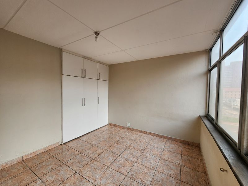 An empty bedroom featuring built-in cupboards, tiled flooring, and large windows providing natural light.