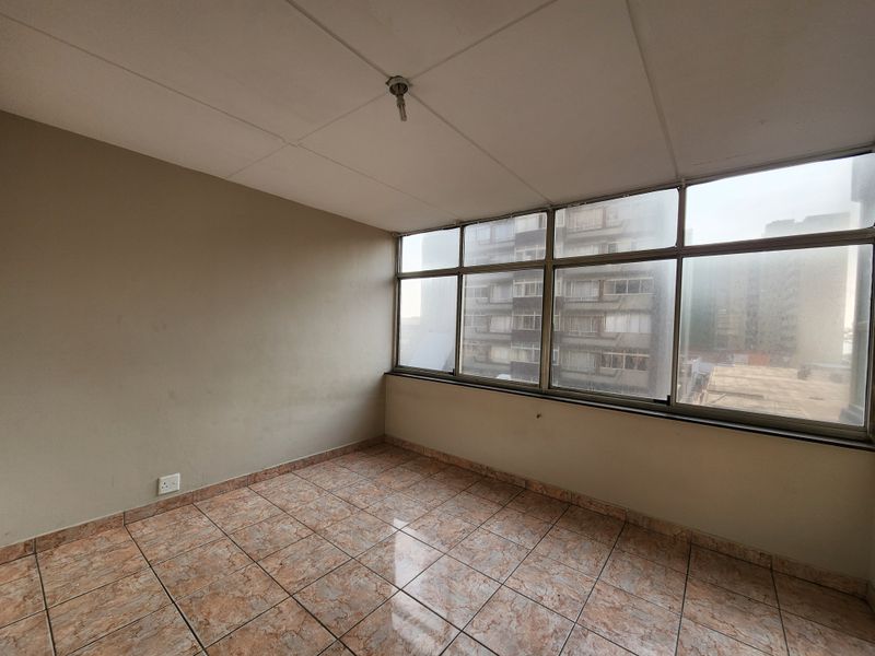 An empty, enclosed balcony area featuring tiled flooring and large windows with urban views, offering potential for a sunroom or study space.