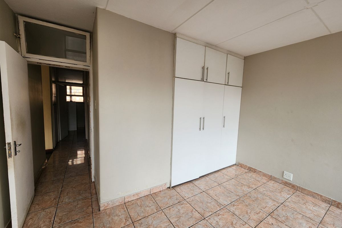 An empty bedroom featuring built-in cupboards, tiled flooring, and a doorway leading to a hallway.