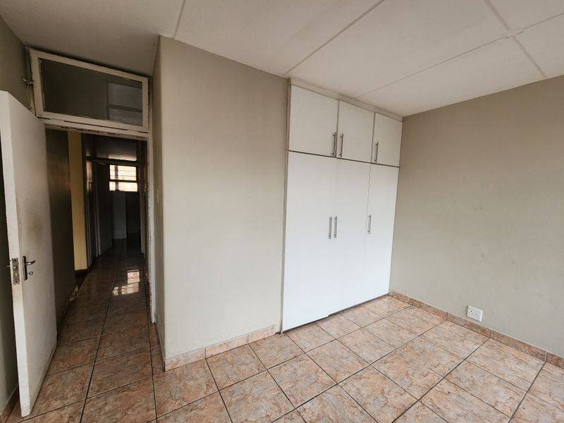 An empty bedroom featuring built-in cupboards, tiled flooring, and a doorway leading to a hallway.