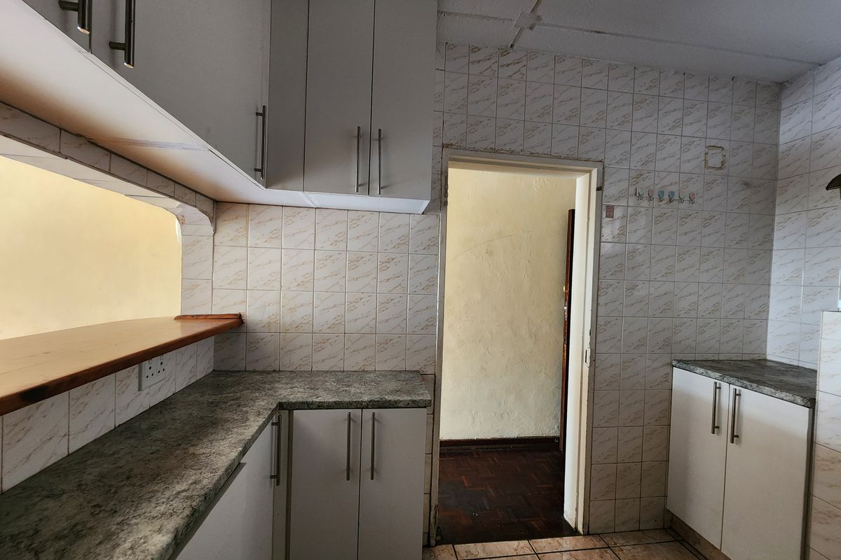 A dated kitchen featuring white cabinetry, laminate countertops, and tiled wall finishes, offering a functional layout ready for modernization.