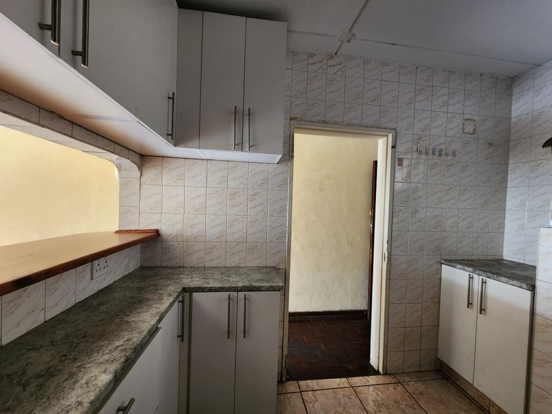 A dated kitchen featuring white cabinetry, laminate countertops, and tiled wall finishes, offering a functional layout ready for modernization.