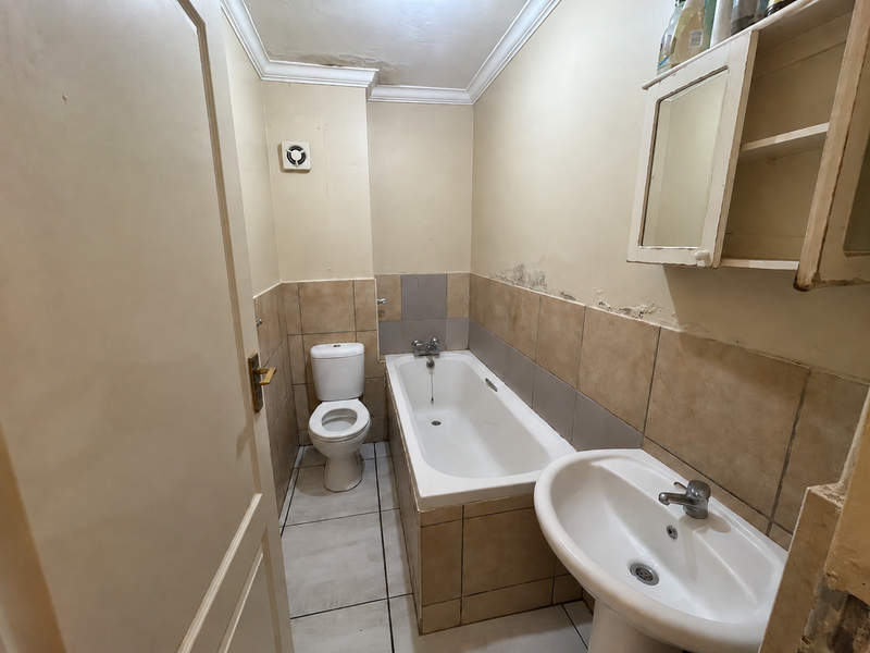 A compact bathroom featuring a bathtub, pedestal basin, and toilet, requiring cosmetic updates and repairs to the wall and ceiling finishes.