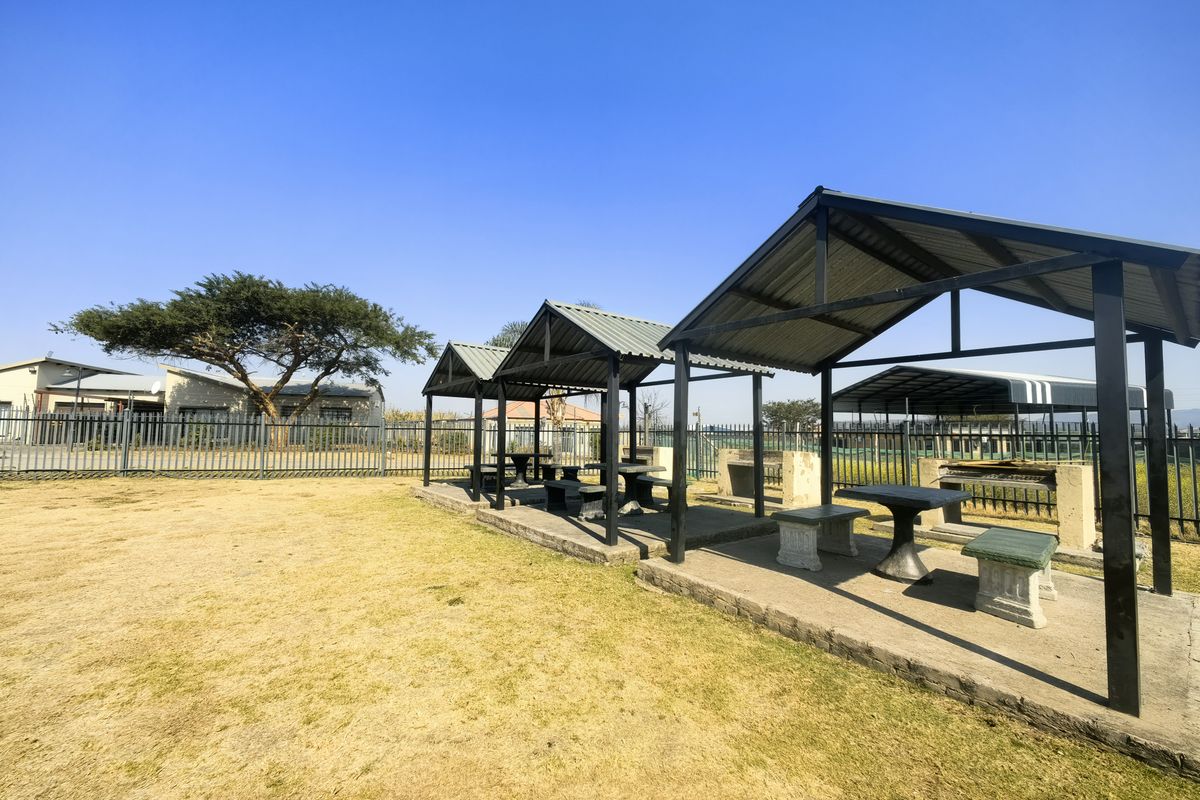 Outdoor communal area featuring covered seating structures with built-in braai facilities and metal perimeter fencing.