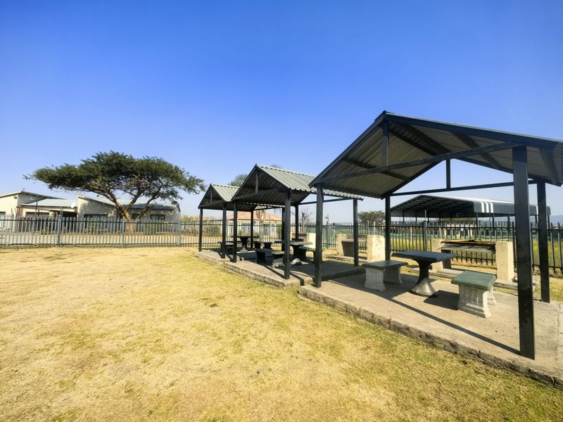 Outdoor communal area featuring covered seating structures with built-in braai facilities and metal perimeter fencing.