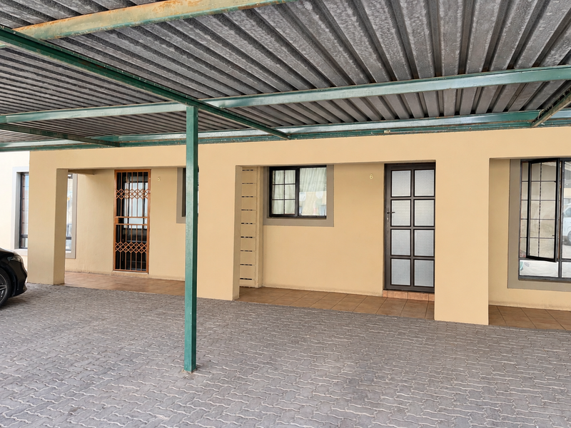 Covered parking area featuring a corrugated metal roof, paved driveway, and direct access to apartment units with security gates and glass doors.