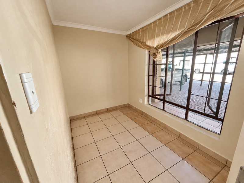 An empty, tiled room featuring a large metal-framed window with views of the exterior parking area.