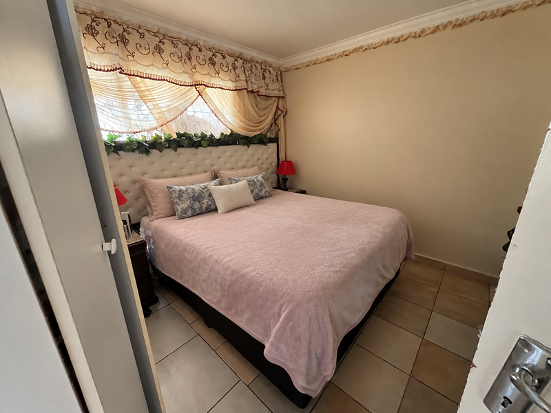A cozy bedroom featuring tiled flooring, crown molding, and a tufted upholstered headboard, offering a comfortable and functional sleeping space.