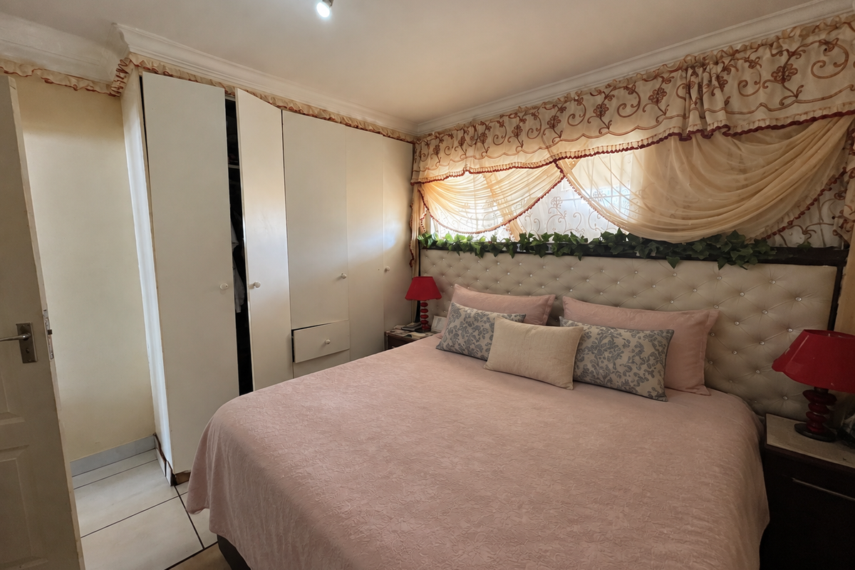 A bedroom featuring built-in cupboards, tiled flooring, and a decorative upholstered headboard with integrated lighting.