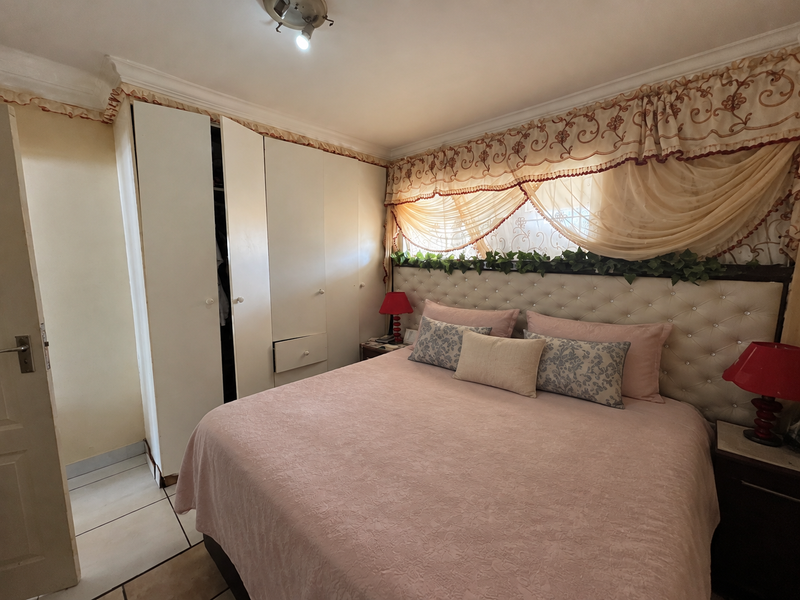 A bedroom featuring built-in cupboards, tiled flooring, and a decorative upholstered headboard with integrated lighting.