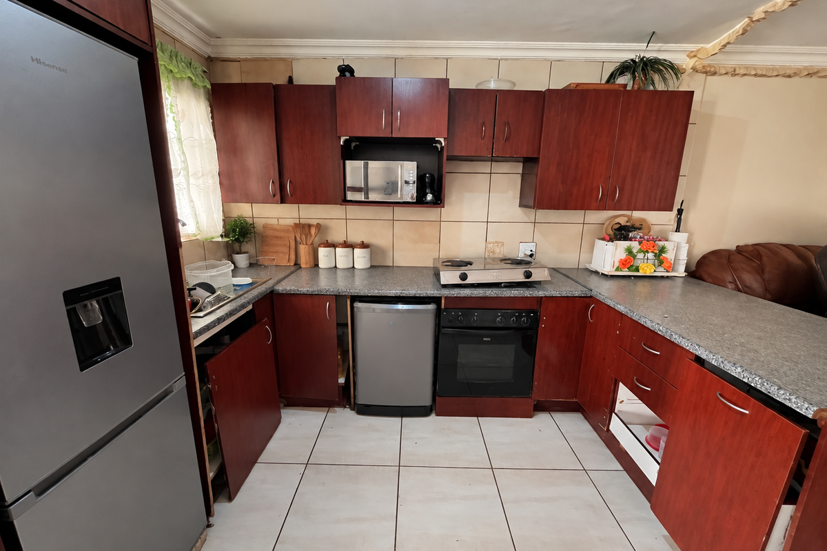 A functional kitchen featuring dark wood cabinetry, granite-look laminate countertops, a gas hob, and built-in oven, with tiled flooring and backsplash throughout.