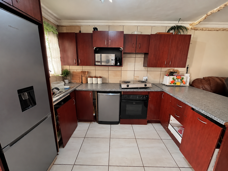 A functional kitchen featuring dark wood cabinetry, granite-look laminate countertops, a gas hob, and built-in oven, with tiled flooring and backsplash throughout.