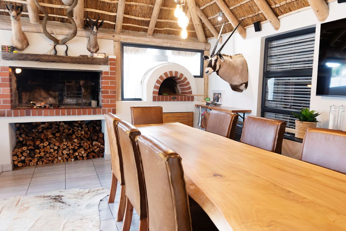Rustic living area featuring a high thatched ceiling with exposed beams, a built-in brick fireplace, and a traditional pizza oven.