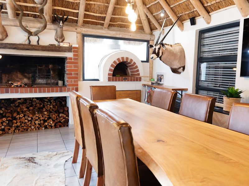 Rustic living area featuring a high thatched ceiling with exposed beams, a built-in brick fireplace, and a traditional pizza oven.