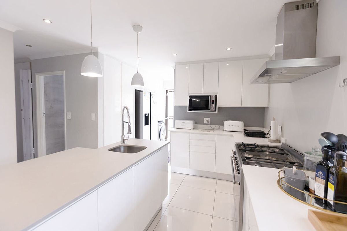 Modern kitchen featuring a central island with sink, sleek white cabinetry, stone countertops, gas cooktop, and high-quality stainless steel appliances.
