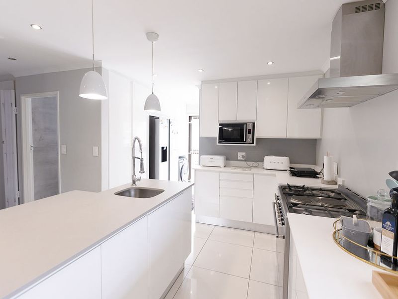 Modern kitchen featuring a central island with sink, sleek white cabinetry, stone countertops, gas cooktop, and high-quality stainless steel appliances.
