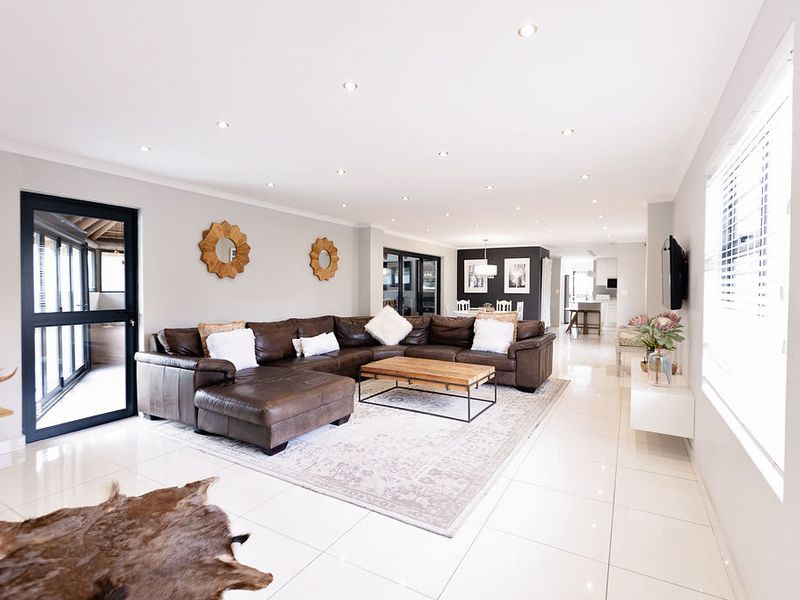 Spacious open-plan living area featuring polished porcelain floor tiles, recessed downlighting, and large aluminium-framed glass doors leading to the outdoor space.