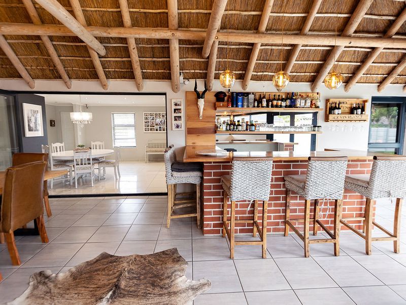 Spacious entertainment area featuring a built-in brick bar with timber counter, exposed thatch ceiling, and seamless flow to the adjacent dining room.