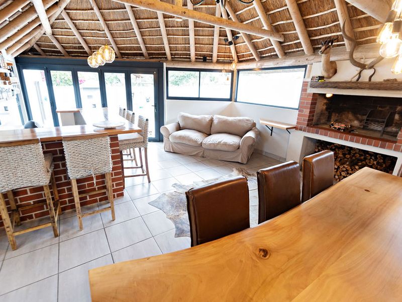 Spacious open-plan entertainment area featuring a high thatched ceiling with exposed rafters, a built-in brick fireplace, and a custom brick bar counter.